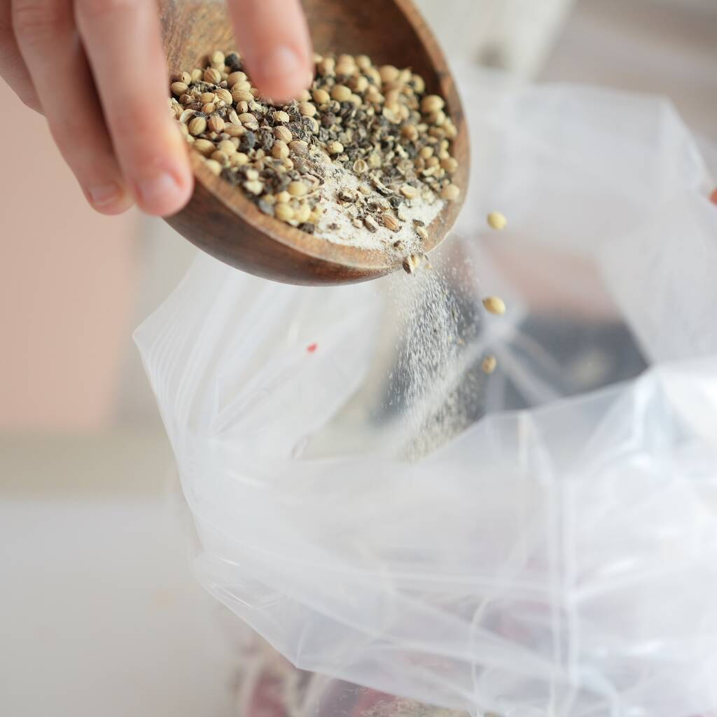 A person pouring natural ingredient spices from a wooden bowl into a clear plastic bag for seasoning. Beef Sticks - Vacuum Sealed biltong 