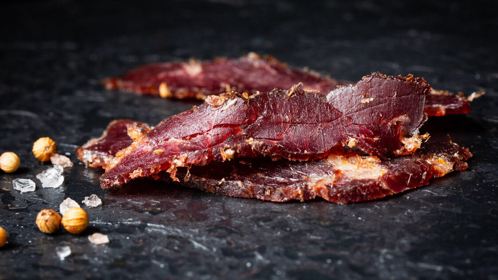 Chilli - Sliced Biltong pieces on a dark stone surface with spices.