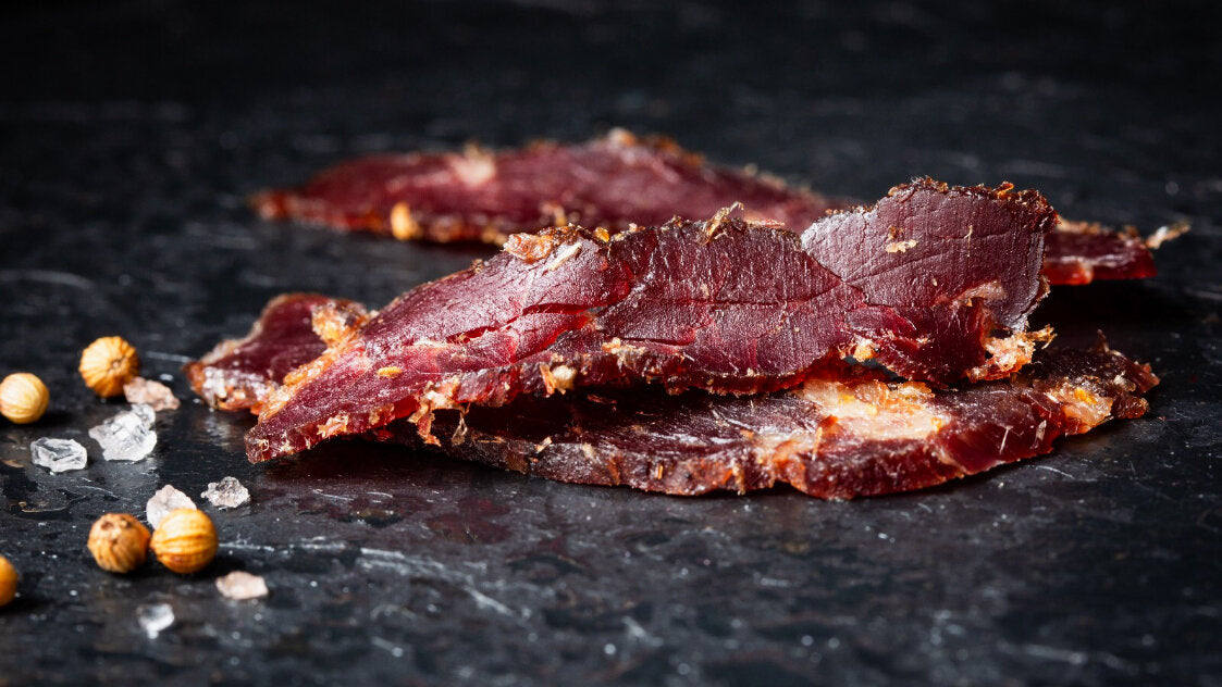 Chilli - Sliced Biltong pieces on a dark stone surface with spices.